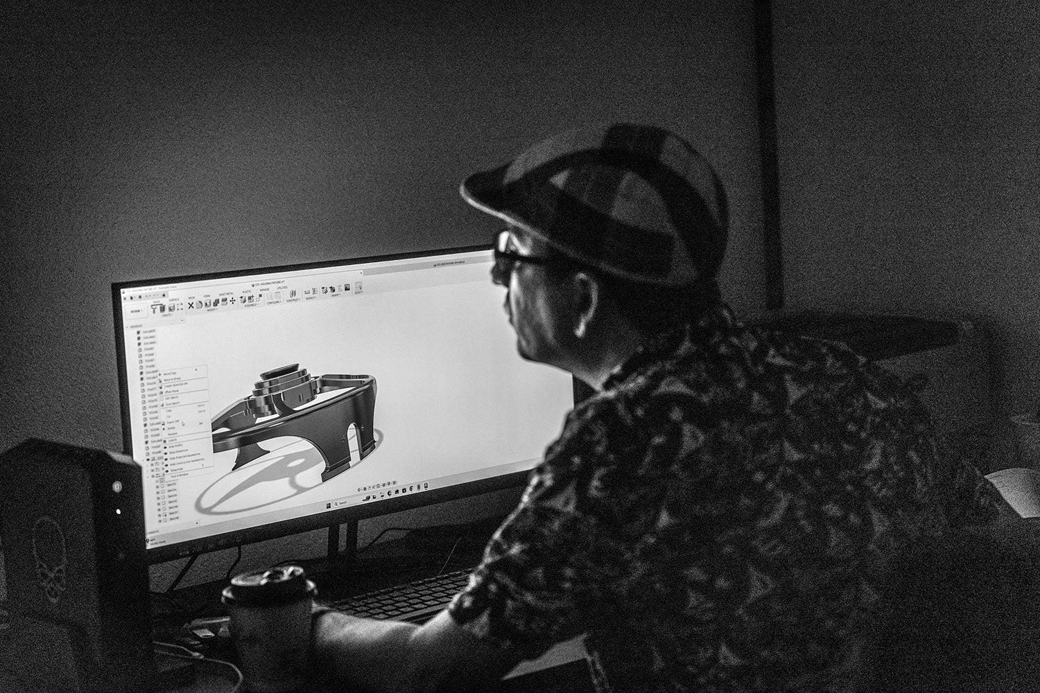 Person working on a computer with 3D modeling software in a dimly lit room.