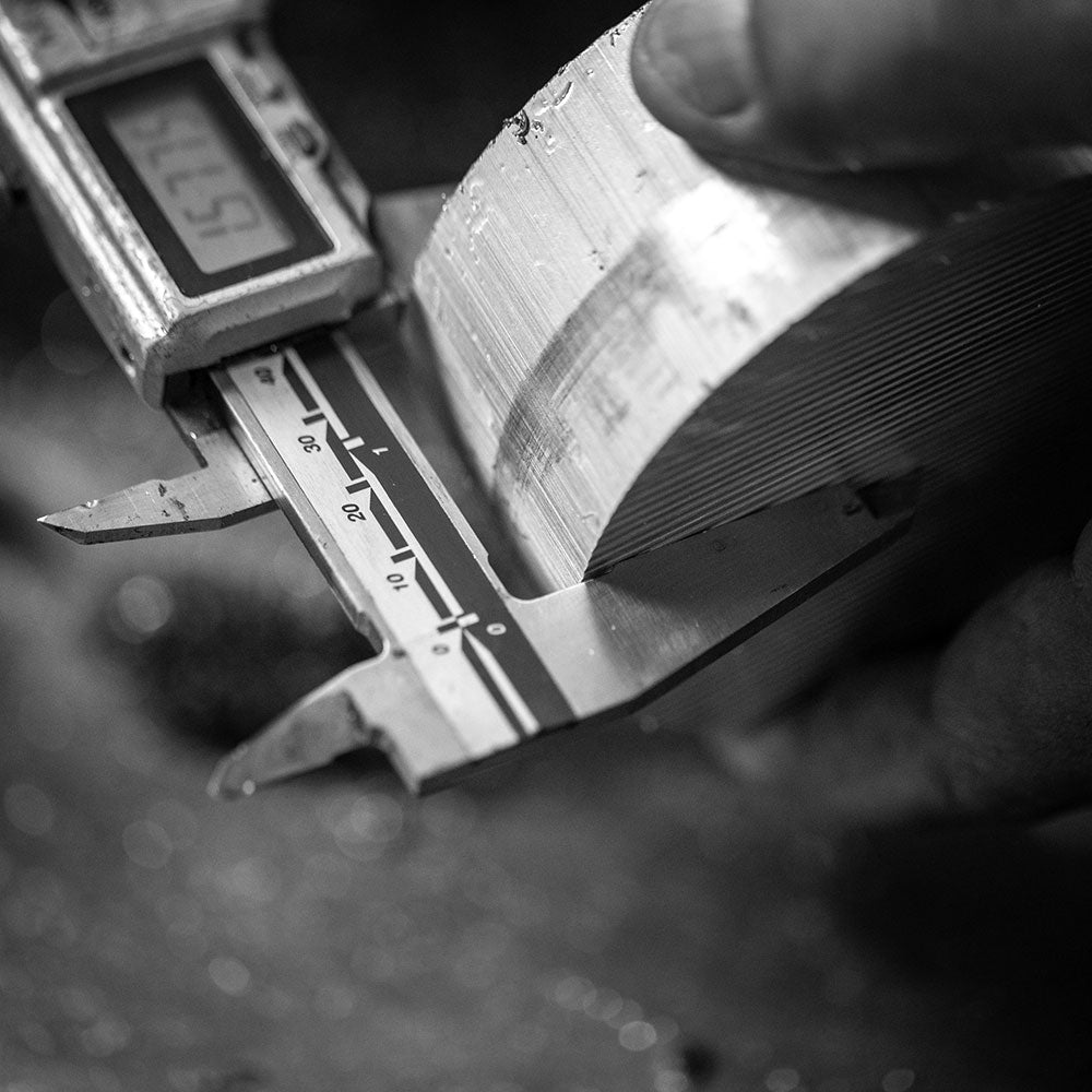 Close-up of a hand holding a metallic object next to a digital caliper on a textured surface.